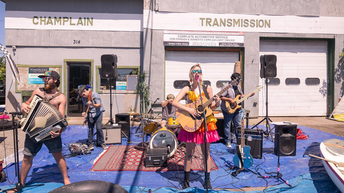 A band dressed in colorful clothing performs in front of a former auto repair shop.