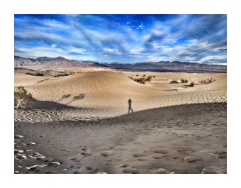 A photograph of a figure walking across dunes in the desert 