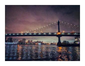 A photograph of of the Manhattan Bridge at dusk with the lights reflected in the water