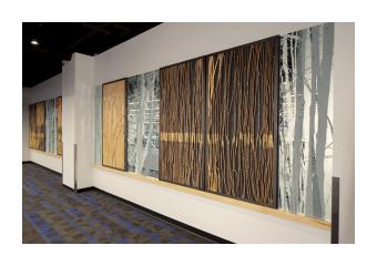 Photo of wooden artpiece hung in long hallway, mirroring a forest.