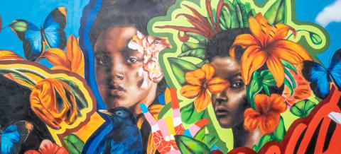 A closeup of a mural featuring a portrait of two girls and bright blooms of flowers against a sky-blue background with "A Love Supreme" written beneath them.