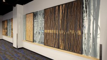 Photo of wooden artpiece hung in long hallway, mirroring a forest.