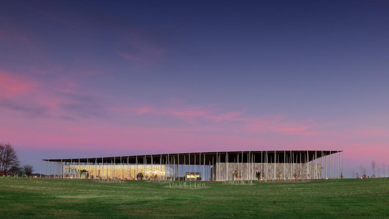 An image of a long, flat building against a cotton candy sunset above a bright green lawn.