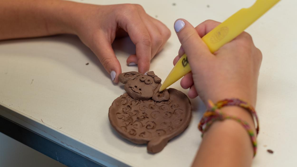 Childrens hands working with a piece of clay in the shape of an animal using a plastic yellow tool.