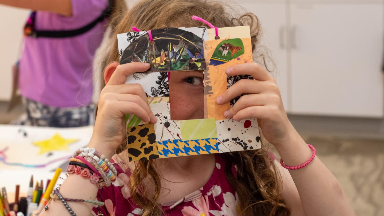 Child holding piece of art over the.ir face with their eye peeking through